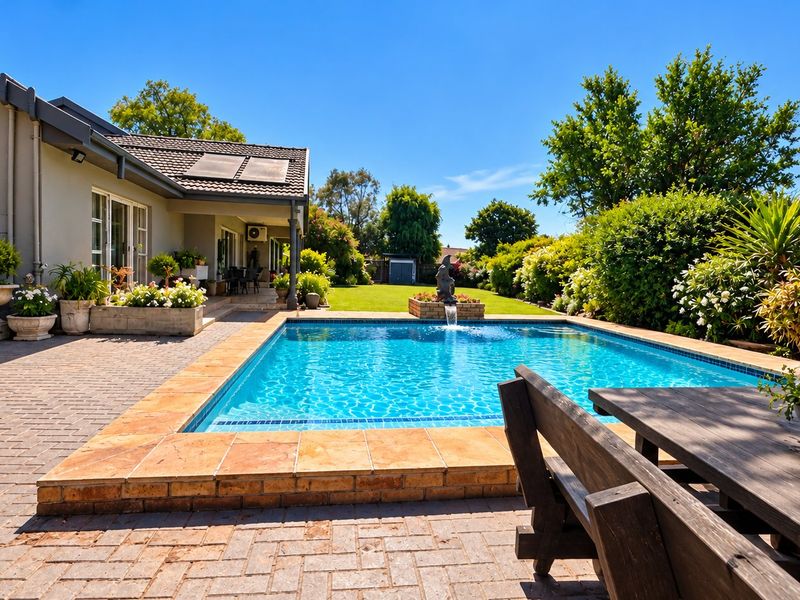 A well-maintained outdoor pool area featuring a paved patio, integrated water feature, and established garden surroundings, perfect for outdoor relaxation and entertainment.