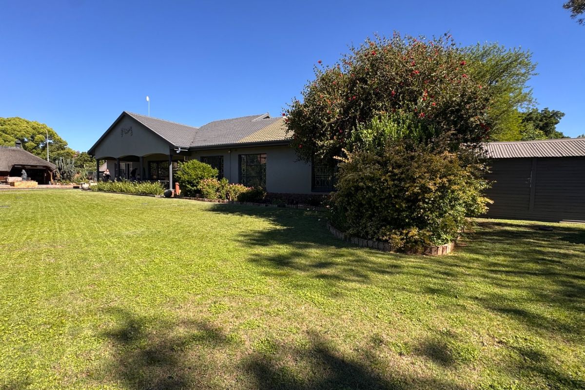 Spacious rear exterior view featuring a well-maintained lawn, established garden, covered patio area, and attached garage structure.