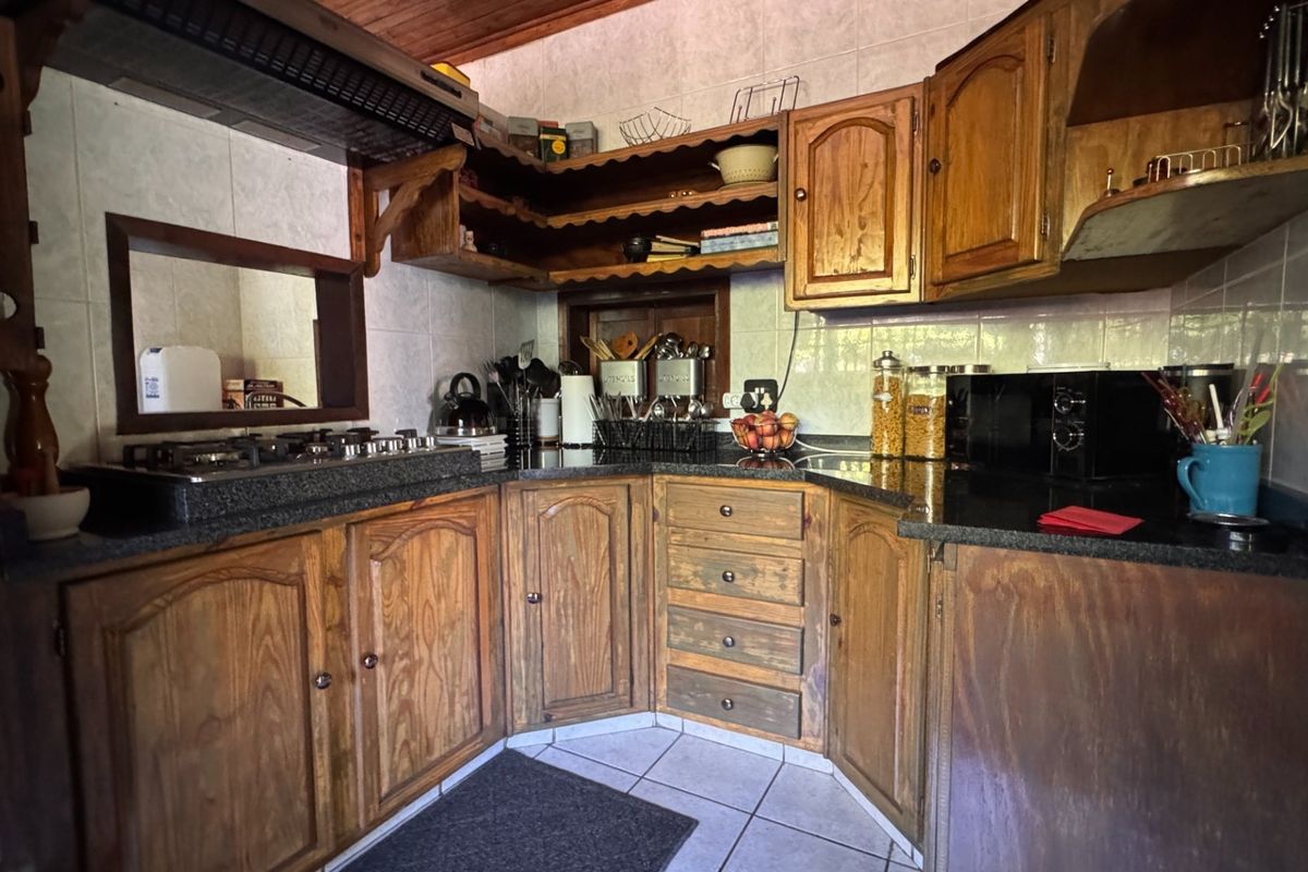 A functional kitchen featuring wooden cabinetry, granite countertops, a gas hob with extractor fan, and tiled finishes throughout.