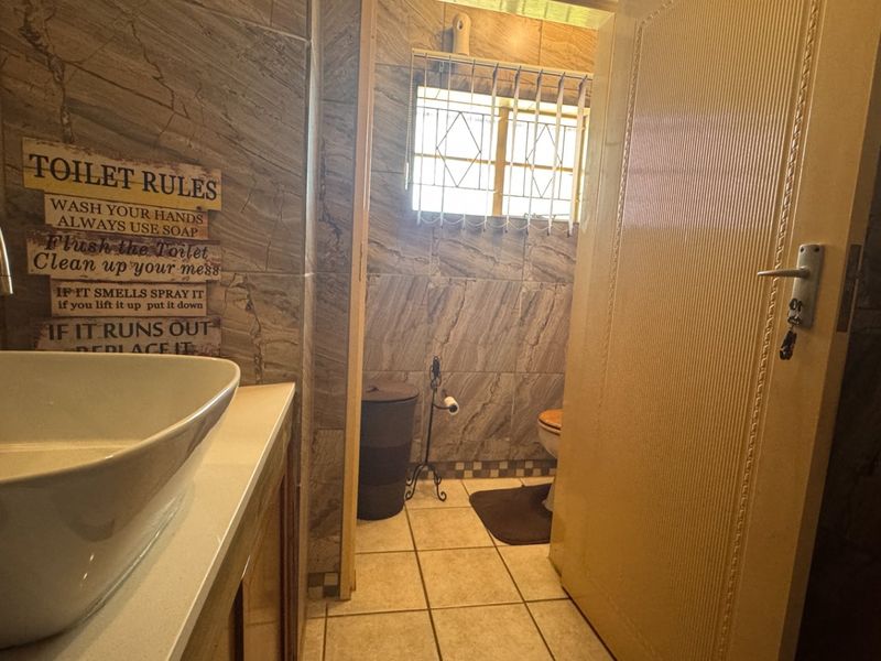 A functional bathroom featuring tiled walls and flooring, a modern vessel sink, and a window with security bars.