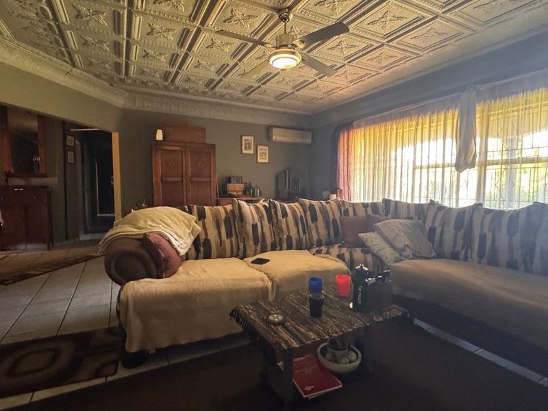 Spacious living room featuring a decorative pressed metal ceiling, ceiling fan, split-system air conditioning, and tiled flooring with large windows protected by security bars.