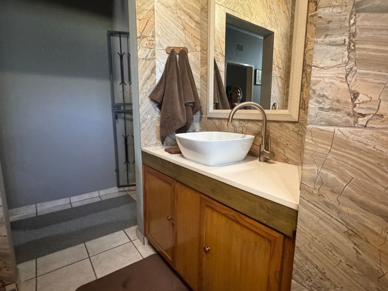 A bathroom vanity area featuring a vessel sink, modern faucet, wooden cabinetry, and decorative stone-look wall tiling.