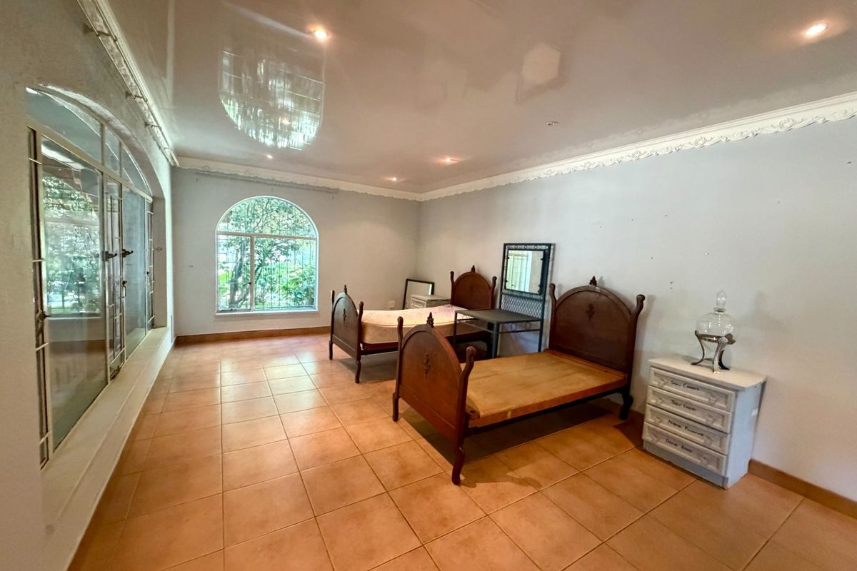 Spacious bedroom featuring large arched windows, tiled flooring, and decorative ceiling cornicing, offering a bright and airy atmosphere with potential for modern updates.