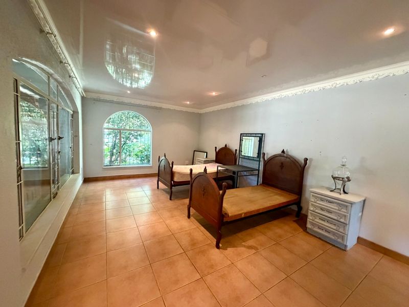 Spacious bedroom featuring large arched windows, tiled flooring, and decorative ceiling cornicing, offering a bright and airy atmosphere with potential for modern updates.