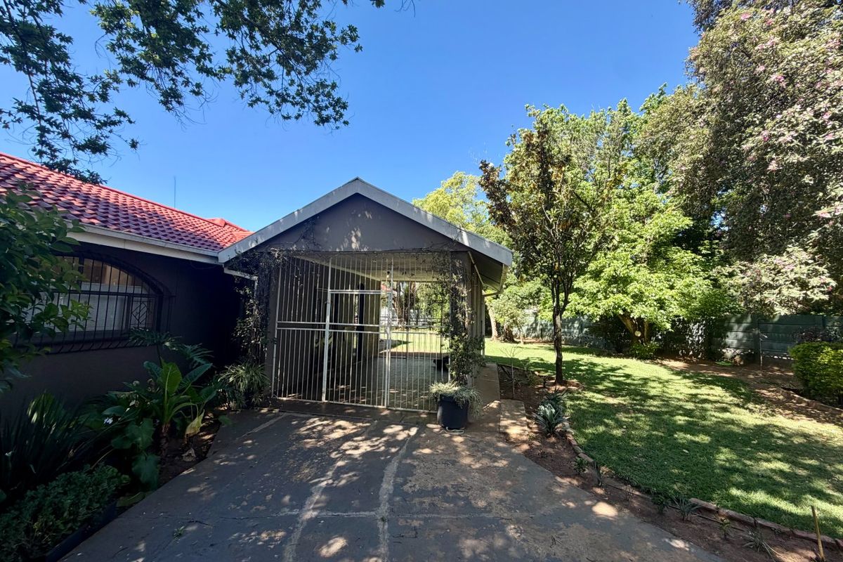 Rear view of the property featuring a covered patio area with security gate, concrete driveway, and a spacious established garden.