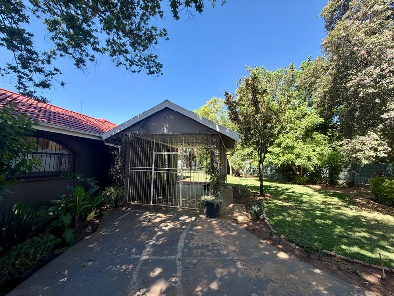 Rear view of the property featuring a covered patio area with security gate, concrete driveway, and a spacious established garden.