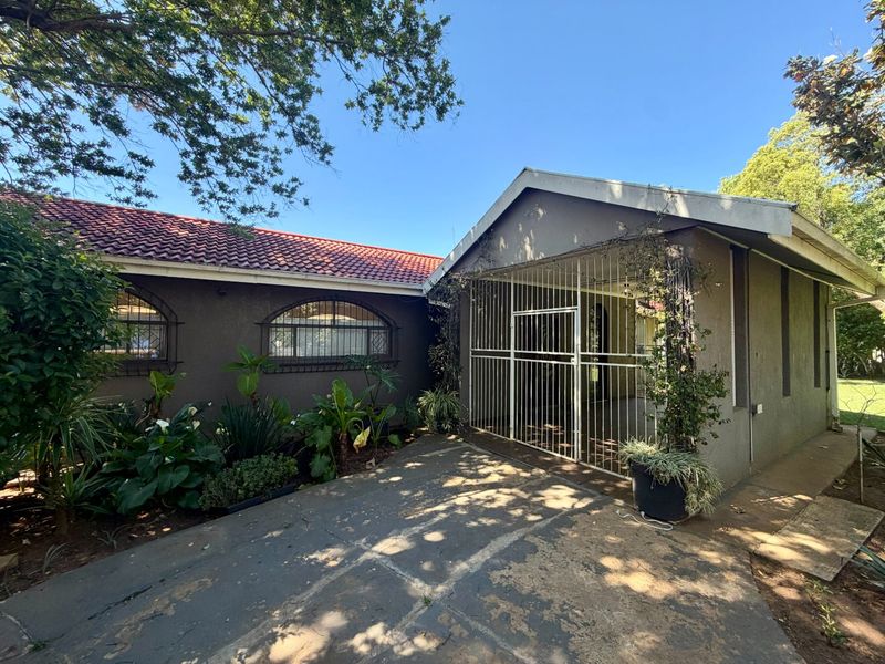 Front exterior view of the house featuring a tiled roof, security gate, and a concrete driveway with established garden beds.