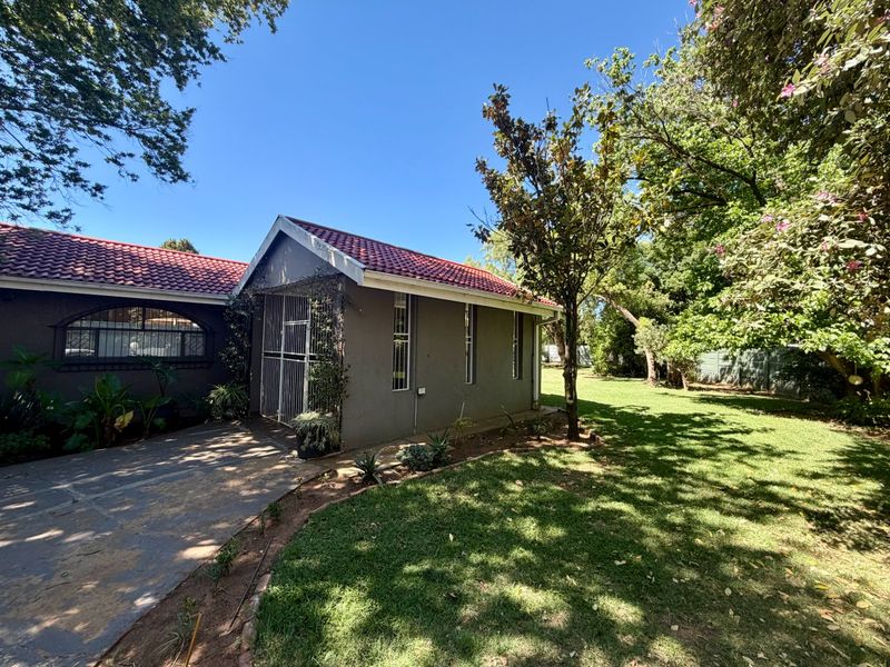 Rear view of the property featuring a tiled roof, security gates, and a spacious garden with a paved driveway area.