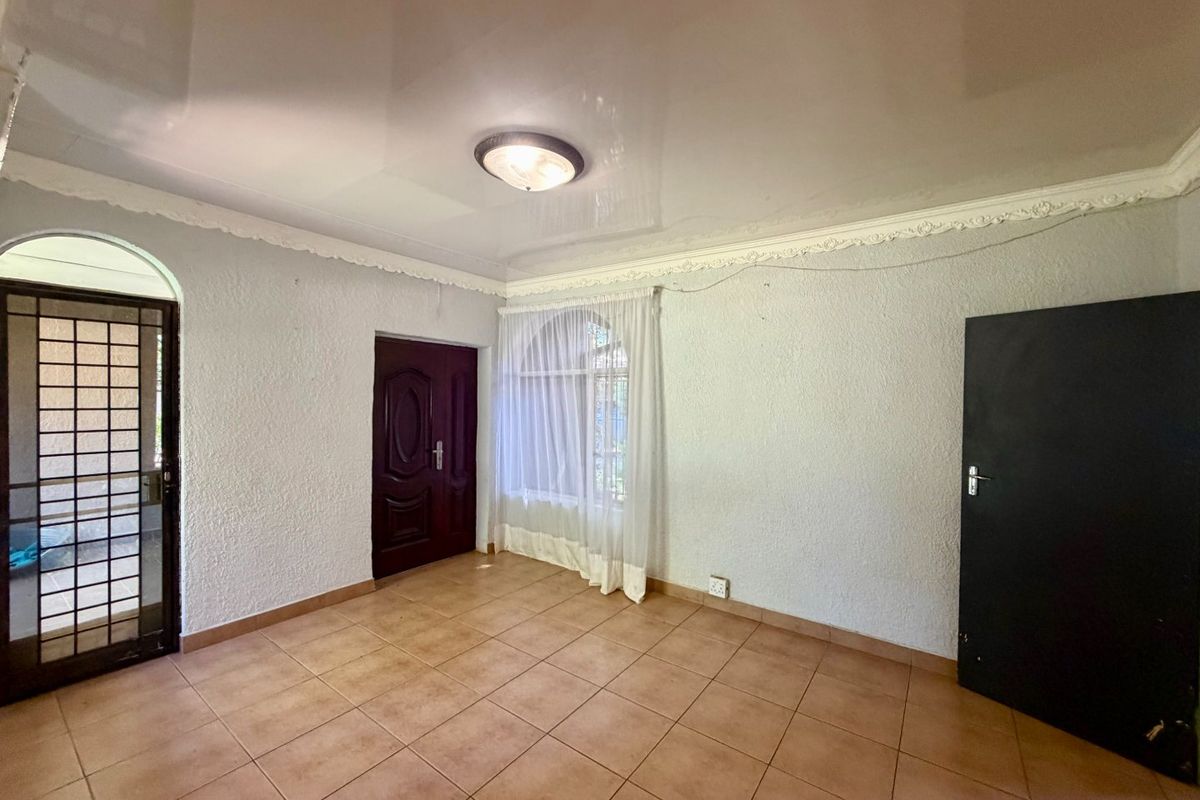 An empty living area featuring ceramic floor tiles, decorative ceiling cornices, and an arched window with a security gate at the entrance.