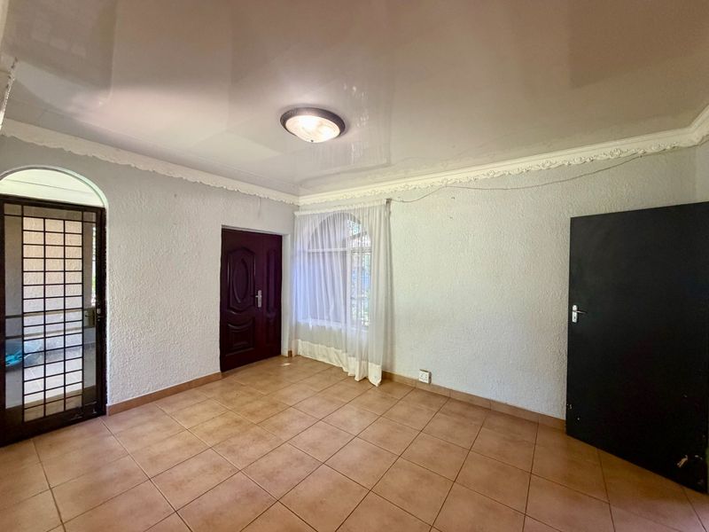 An empty living area featuring ceramic floor tiles, decorative ceiling cornices, and an arched window with a security gate at the entrance.