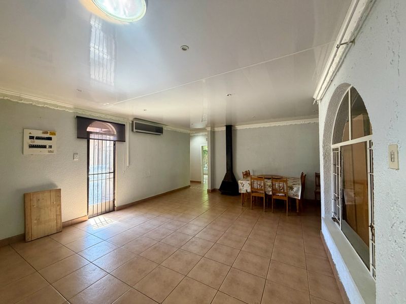 Spacious living area featuring tiled flooring, a freestanding fireplace, air conditioning, and an arched window with security gate access.