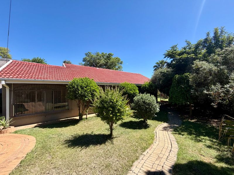 A well-maintained rear exterior view featuring a red tiled roof, established garden, and a brick paved pathway leading through the yard.