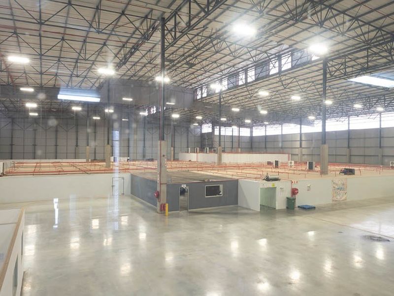 A large, open-plan industrial warehouse space featuring high ceilings with exposed steel trusses, polished concrete floors, and integrated internal office structures.