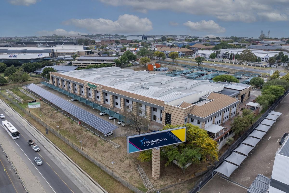 Aerial view of a large industrial property featuring extensive solar panel carports, paved parking, and perimeter security fencing.