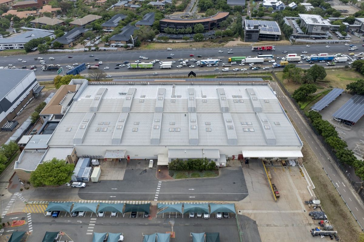 Aerial view of a large industrial warehouse facility featuring a metal roof with skylights, dedicated loading bays, and extensive paved parking with shade structures.