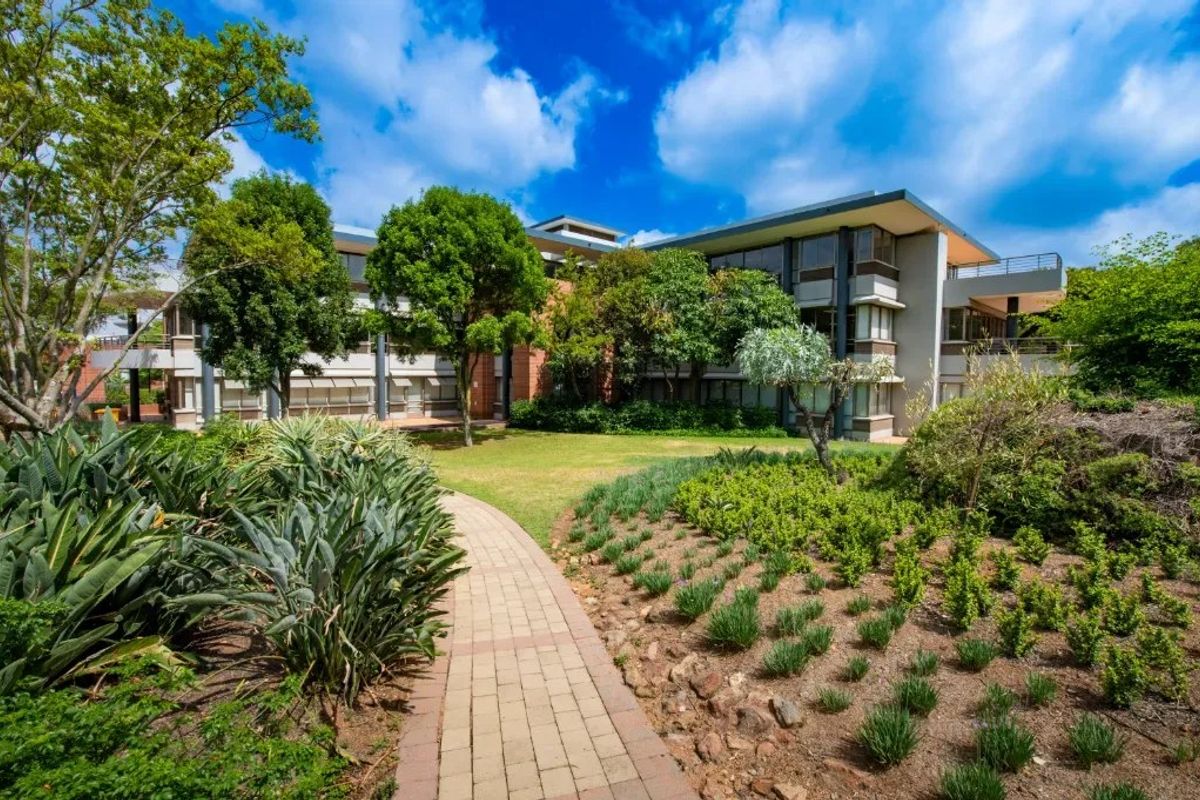A well-maintained commercial building exterior featuring a paved garden walkway, landscaped grounds, and multi-level office facades with balconies.