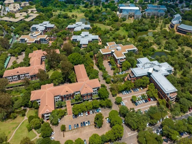 Aerial view of a commercial office park featuring multiple buildings with tiled roofs, extensive landscaped grounds, and dedicated paved parking areas.