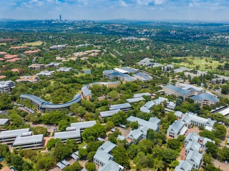 Aerial view of a sprawling commercial office park complex featuring multiple buildings, extensive green landscaping, and integrated parking facilities within a suburban setting.