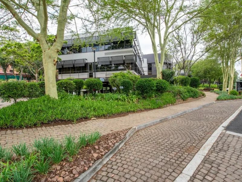 Exterior view of a multi-story commercial office building featuring modern glass facade, external sun shades, and well-maintained landscaped grounds with paved access.