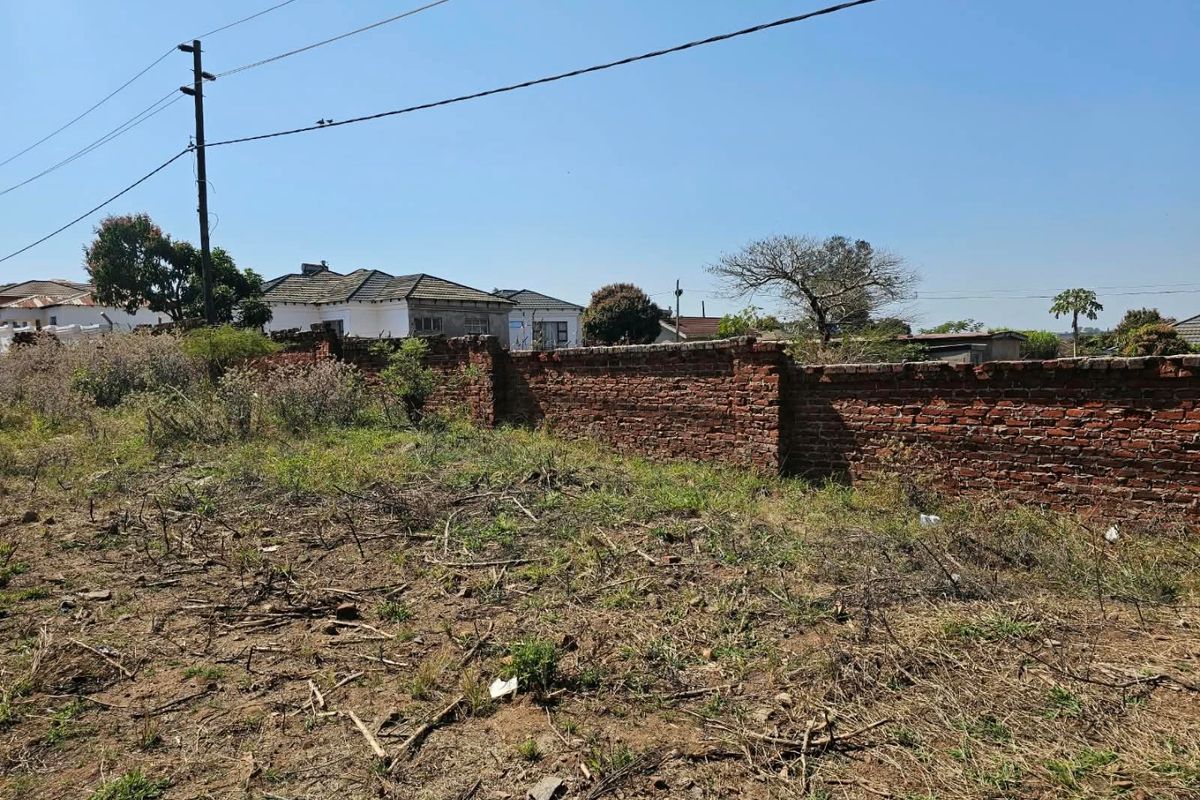 A vacant residential plot featuring a weathered brick boundary wall and existing utility infrastructure, set within an established neighborhood.