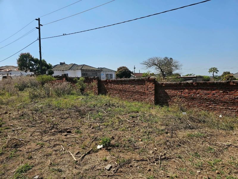 A vacant residential plot featuring a weathered brick boundary wall and existing utility infrastructure, set within an established neighborhood.