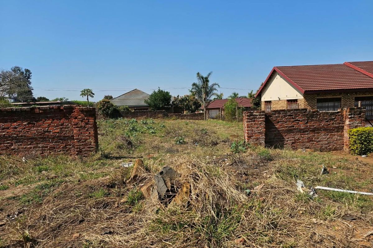 A vacant residential plot featuring an existing brick boundary wall and overgrown vegetation, situated in a developed neighborhood.