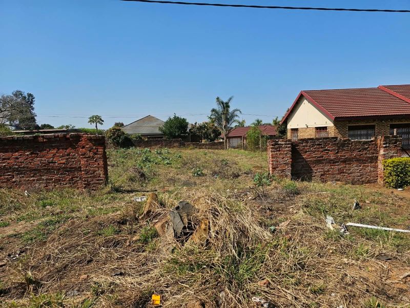 A vacant residential plot featuring an existing brick boundary wall and overgrown vegetation, situated in a developed neighborhood.