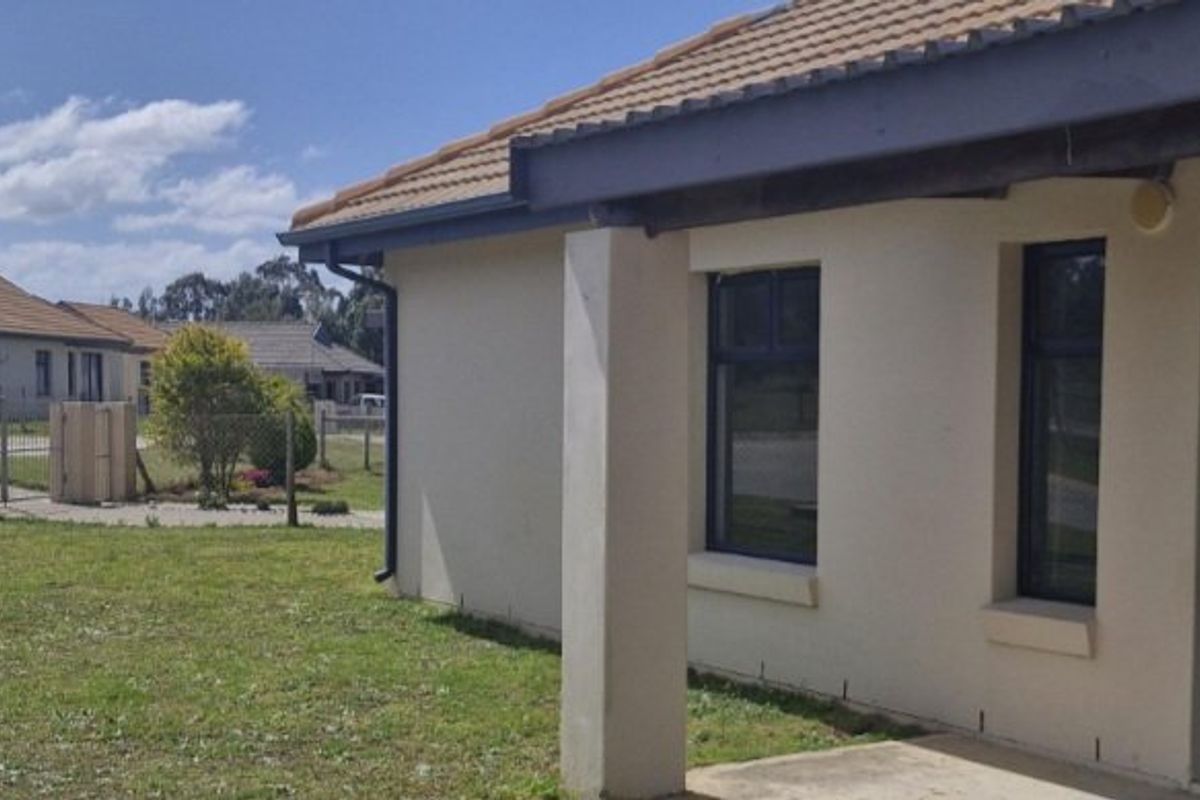 Rear view of the townhouse featuring a concrete patio, tiled roof, and established garden area.