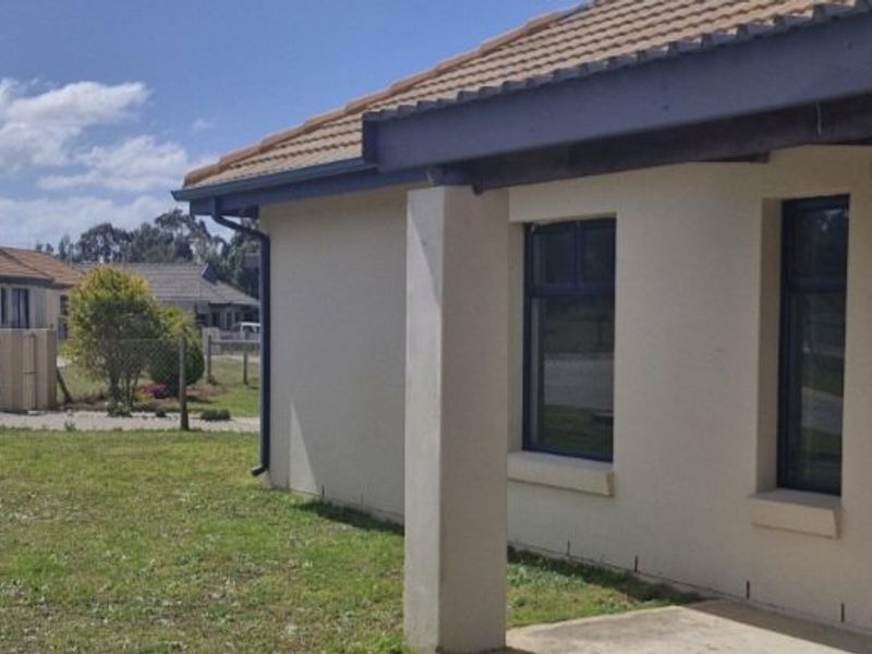 Rear view of the townhouse featuring a concrete patio, tiled roof, and established garden area.
