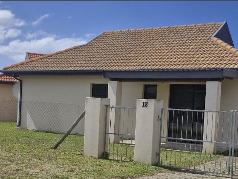Front exterior view of a townhouse featuring a tiled roof, metal gate, and chain link fencing with a paved driveway.
