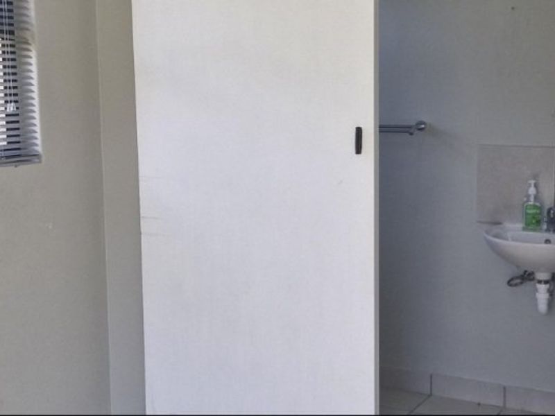 A functional bathroom featuring a wall-mounted basin, towel rail, and venetian blind, presenting a clean and simple layout.
