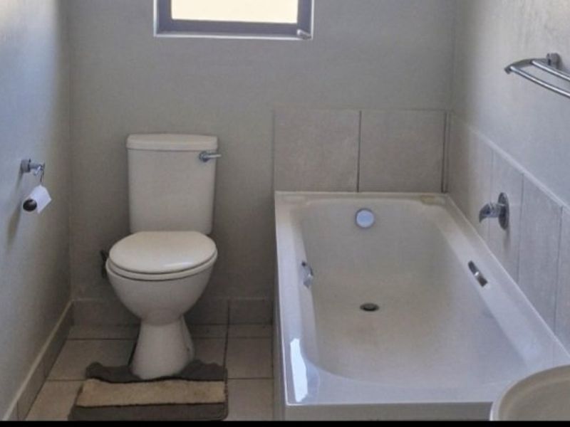 A functional bathroom featuring a standard bathtub, toilet, and neutral tiled finishes, offering a clean and practical space.