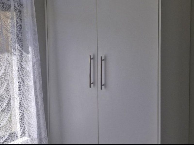 A bedroom featuring a clean, white built-in wardrobe with modern metal handles.