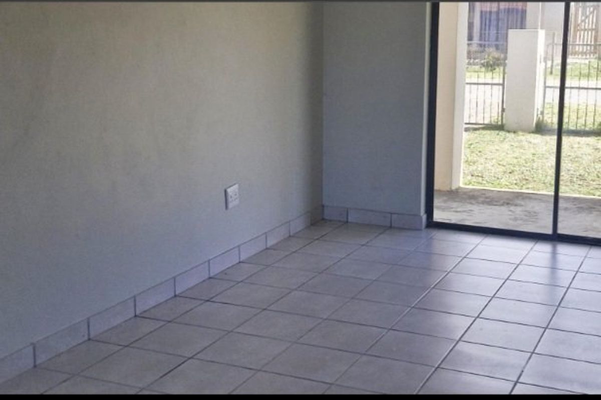 An empty living area featuring neutral tiled flooring, tiled skirting, and a sliding glass door providing access to the exterior.
