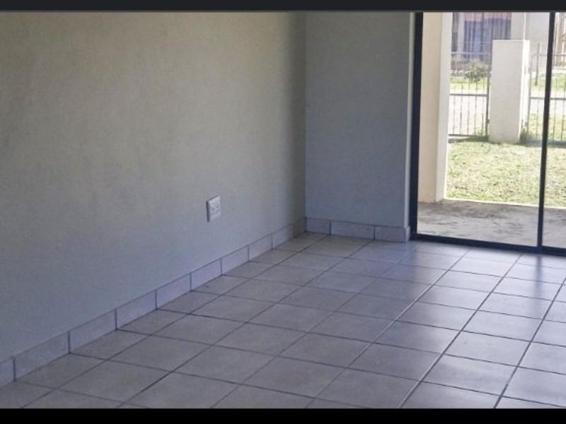 An empty living area featuring neutral tiled flooring, tiled skirting, and a sliding glass door providing access to the exterior.