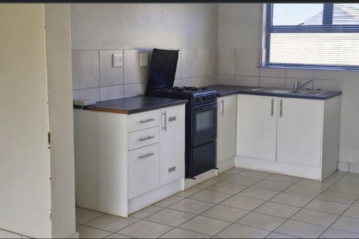 A functional kitchen featuring white cabinetry, laminate countertops, a stainless steel sink, and a freestanding stove with tiled backsplash and flooring.