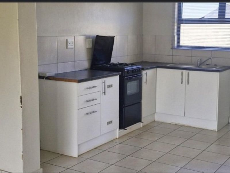 A functional kitchen featuring white cabinetry, laminate countertops, a stainless steel sink, and a freestanding stove with tiled backsplash and flooring.