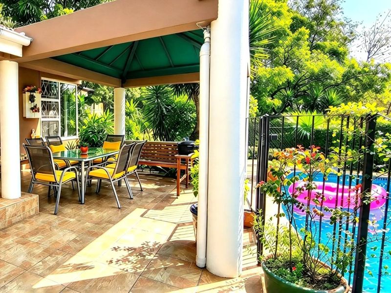 A covered outdoor patio area featuring tiled flooring and support columns, overlooking a private swimming pool with secure metal fencing.