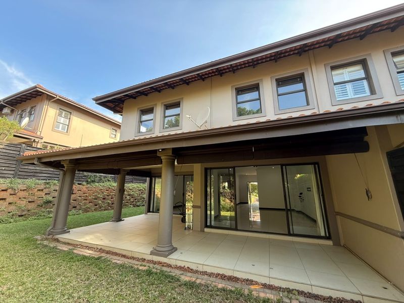 Spacious covered rear patio with tiled flooring, overlooking a landscaped garden and retaining wall, featuring large sliding glass doors leading into the home.
