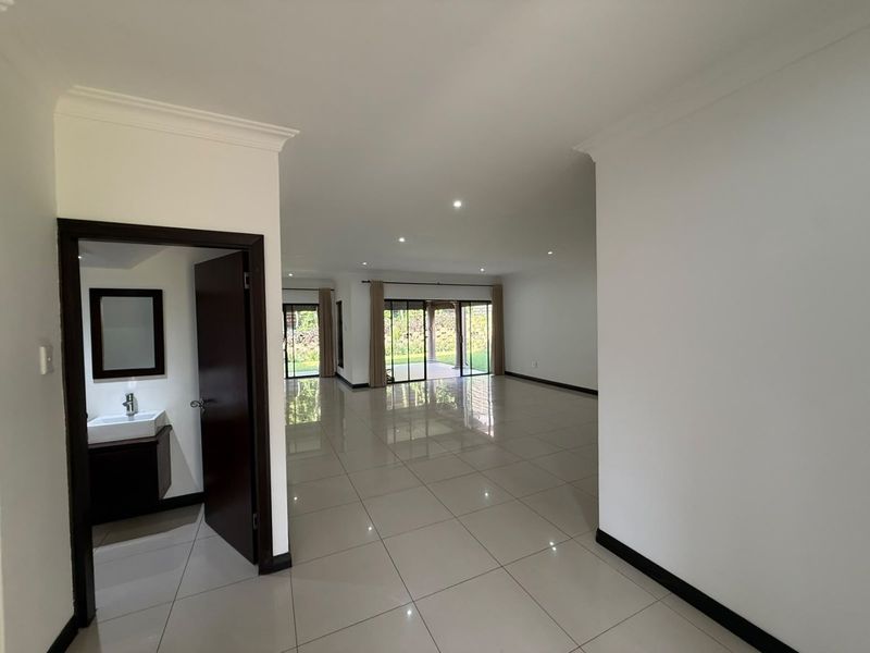 Spacious open-plan living area featuring polished porcelain tiles, recessed lighting, and large sliding doors leading to an outdoor patio, with an adjacent guest bathroom.