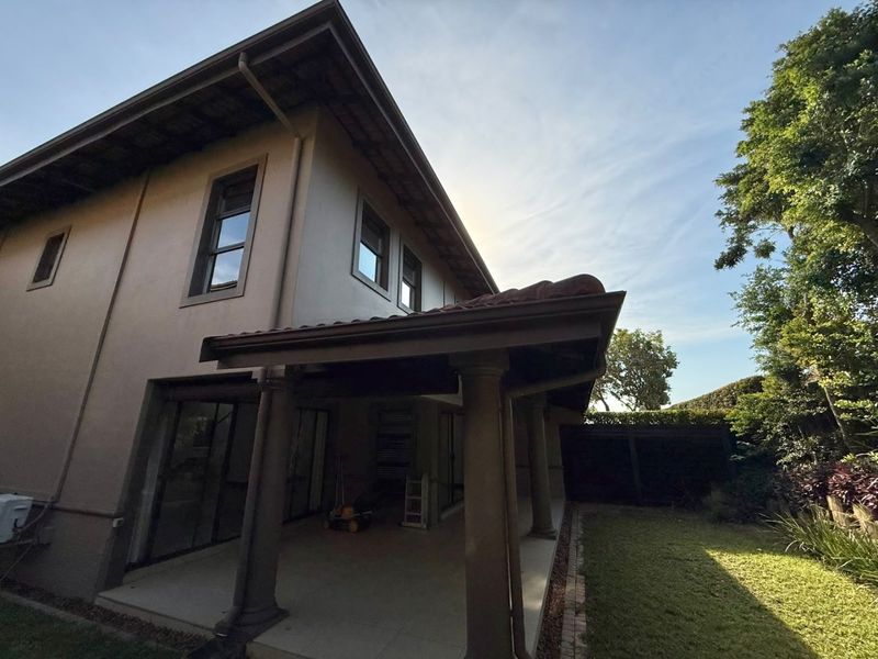 Rear view of the townhouse featuring a covered patio with concrete columns, tiled roof, and sliding glass doors leading to the garden.