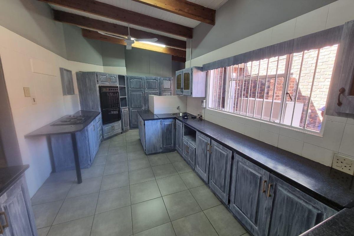 Spacious kitchen featuring exposed timber ceiling beams, extensive built-in cabinetry, dark countertops, and tiled flooring, offering a functional layout with ample storage space.