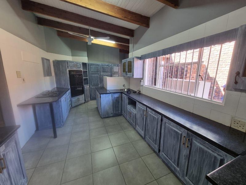 Spacious kitchen featuring exposed timber ceiling beams, extensive built-in cabinetry, dark countertops, and tiled flooring, offering a functional layout with ample storage space.