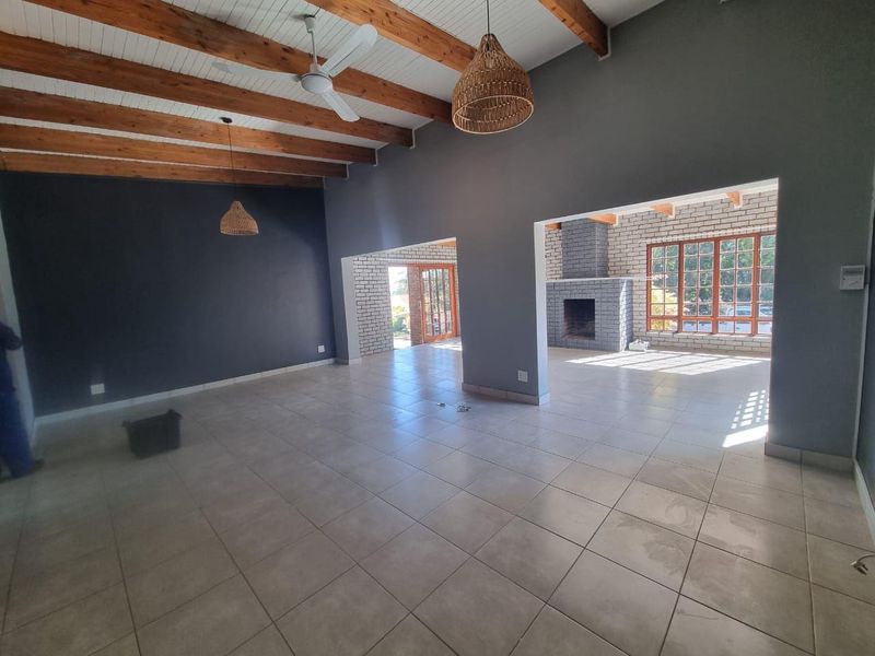 Spacious open-plan living area featuring exposed timber ceiling beams, tiled flooring, and a built-in fireplace, offering a bright and versatile layout.