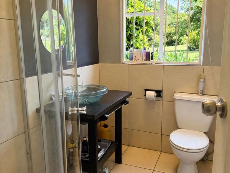 A functional bathroom featuring a glass vessel sink, a shower enclosure, and tiled finishes, with a window providing natural light and garden views.