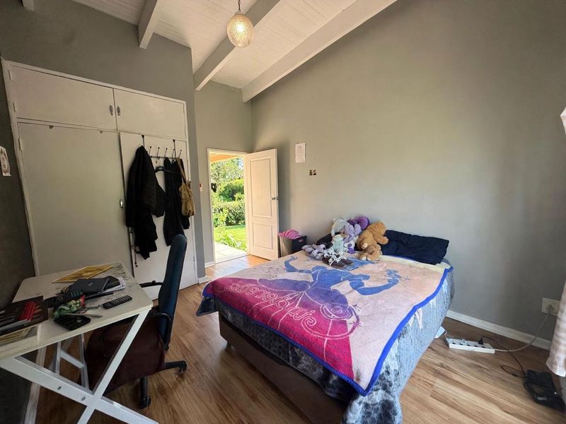 A bedroom featuring laminate flooring, exposed beam ceilings, and built-in cupboards, with direct access to the garden through an external door.