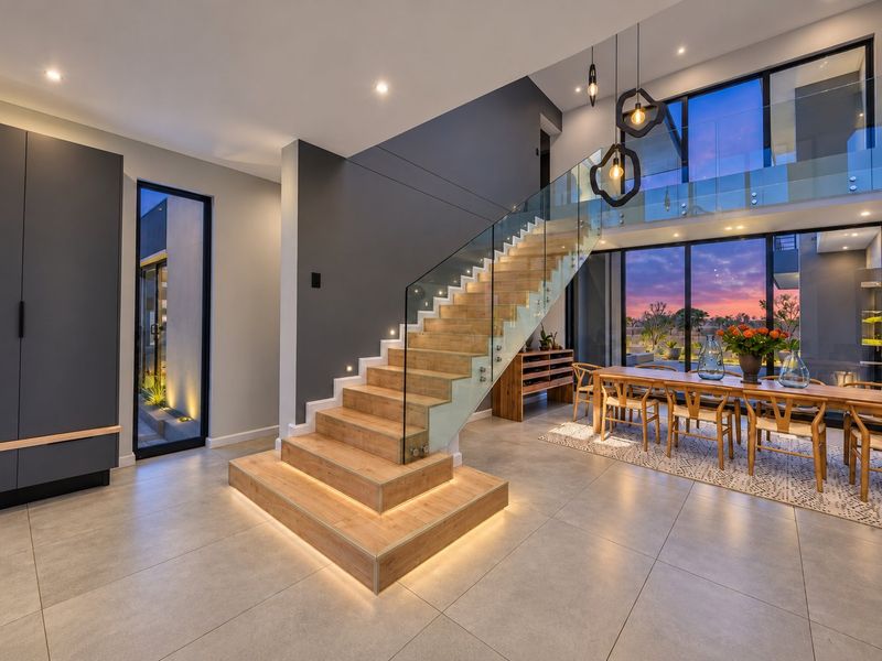 Modern open-plan living area featuring a striking floating staircase with glass balustrades, floor-to-ceiling windows, and high-end contemporary finishes throughout.