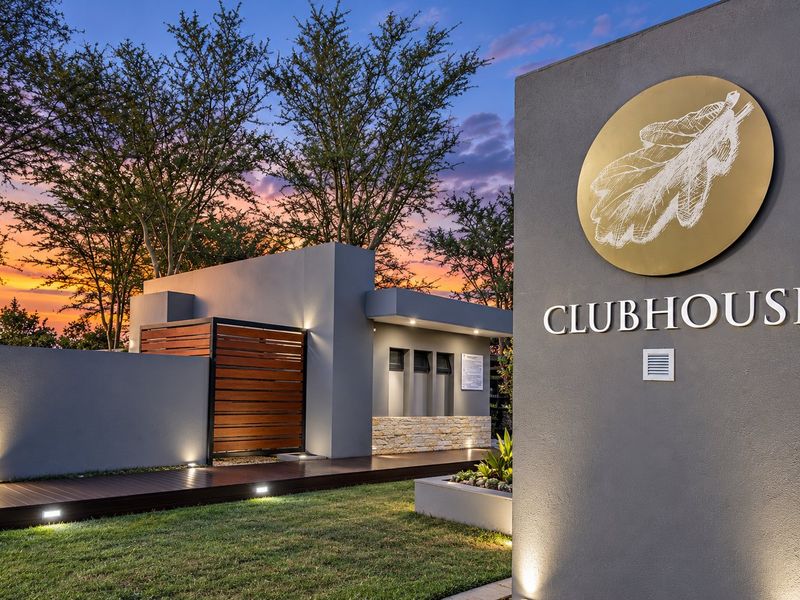 Modern clubhouse entrance featuring contemporary grey facade, timber decking, stone accents, and professional landscape lighting at dusk.