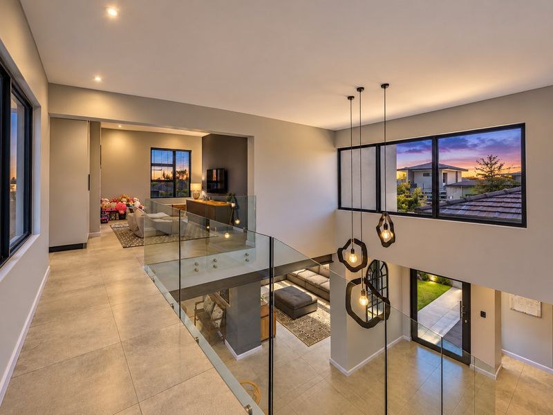 Modern mezzanine hallway featuring a sleek glass balustrade, tiled flooring, and contemporary pendant lighting overlooking the lower living area.