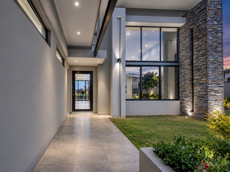 Modern front entrance featuring a tiled walkway, striking stone cladding, and double-volume glass windows, creating a sophisticated and welcoming architectural facade.